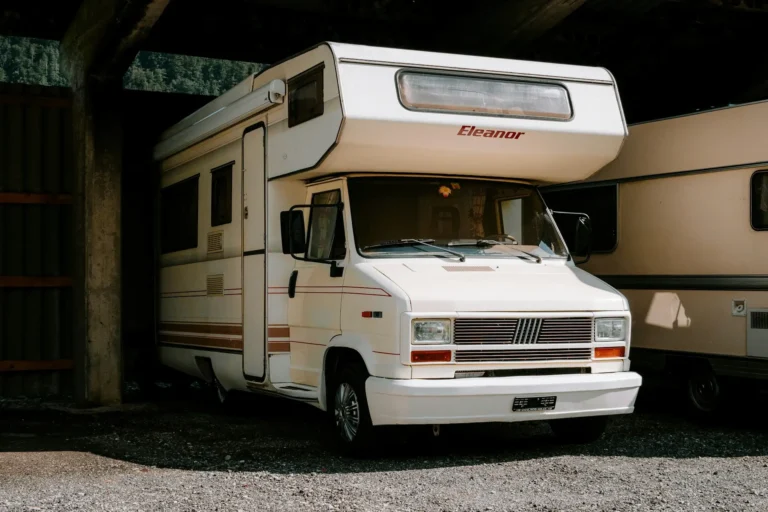 Camping-car blanc « Eleanor » sous un toit métallique sur un sol de gravier.