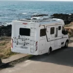 Camping-car blanc stationné près de rochers volcaniques, avec l’océan en arrière-plan.