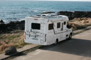 Camping-car blanc stationné près de rochers volcaniques, avec l’océan en arrière-plan.