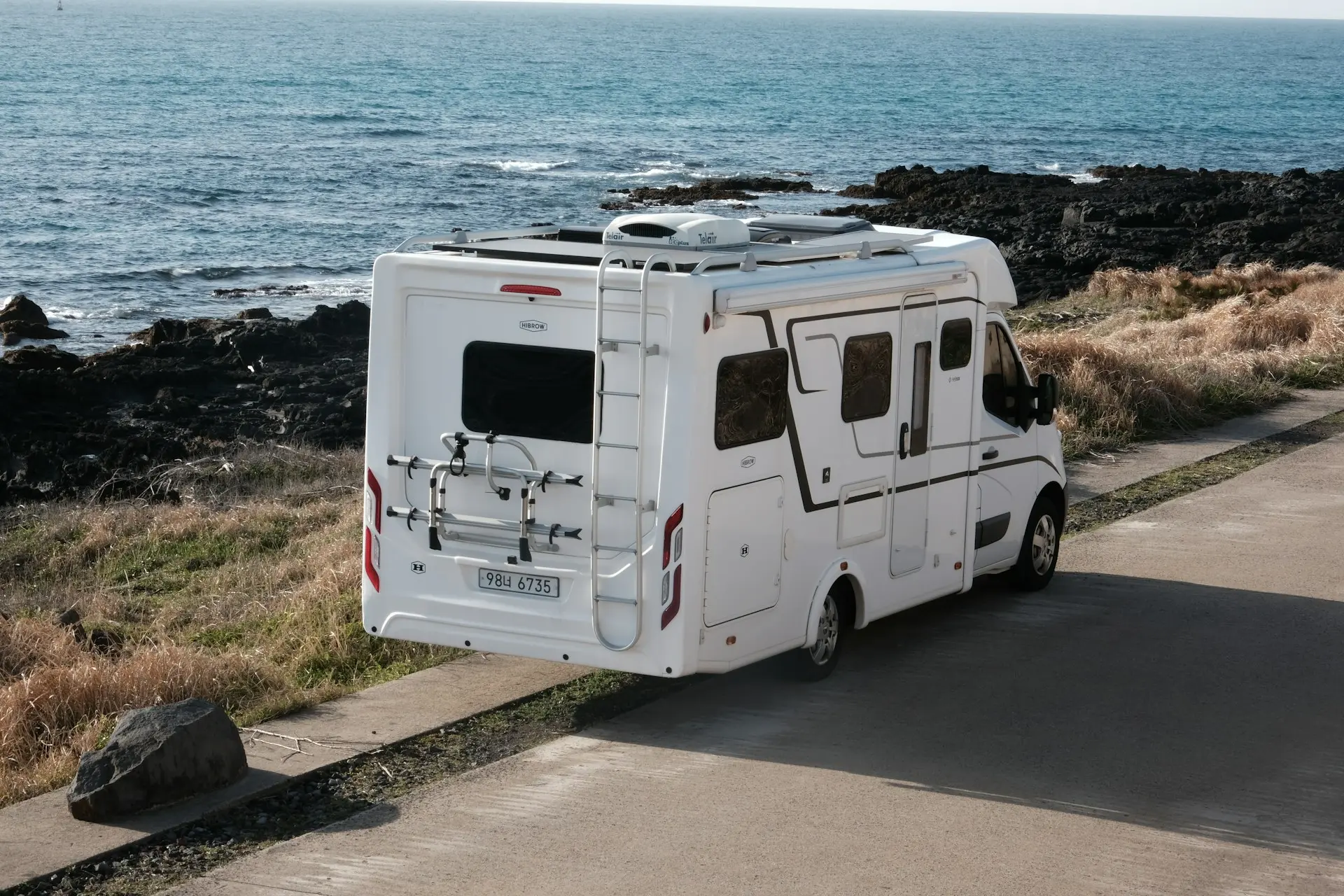 Camping-car blanc stationné près de rochers volcaniques, avec l’océan en arrière-plan.